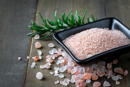 Himalayan Rock pink Salt in black bowl and rosemary leaf  on wood background,