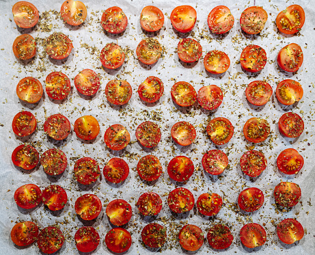 Cooking sun-dried tomatoes, pieces of Cherry tomatoes with herbs and spices on baking sheet high angle view.