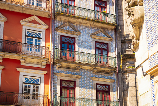 French windows leading out to traditional balconies on the exterior of vibrantly coloured apartments in Porto, Portugal.