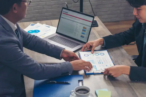 Photo of Two businesspeople meeting work at office desk. Teamwork partners team with Business strategy chart graph, infographic data financial report. Team partner planning marketing finance excel stat report