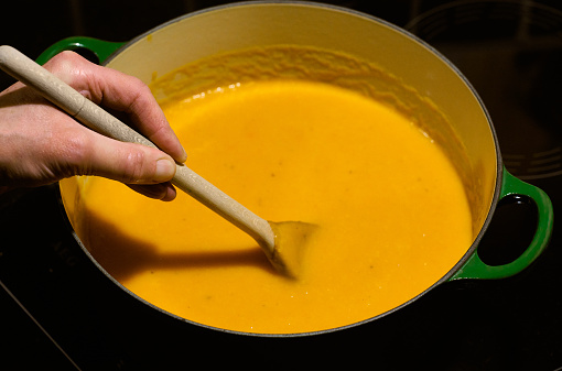 Female hand stirring a pan of carrot soup on an induction hob stove. Recipe is carrots, onion, and rice, with a little thyme.