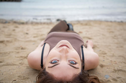 Young woman with blue eyes stretching on the sand at the beach