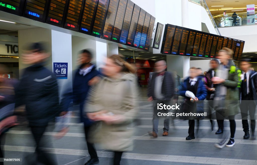 UK railway station concourse. Motion blurred people in front of train information screens in a train station. Color Image Stock Photo