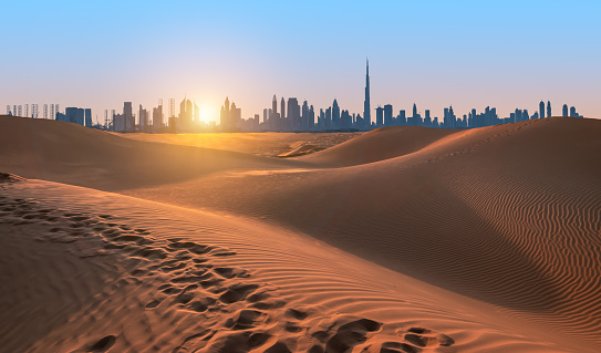 Sand dunes of Dubai, silhouette of Dubai skyline at sunset. Beautiful travel image.
