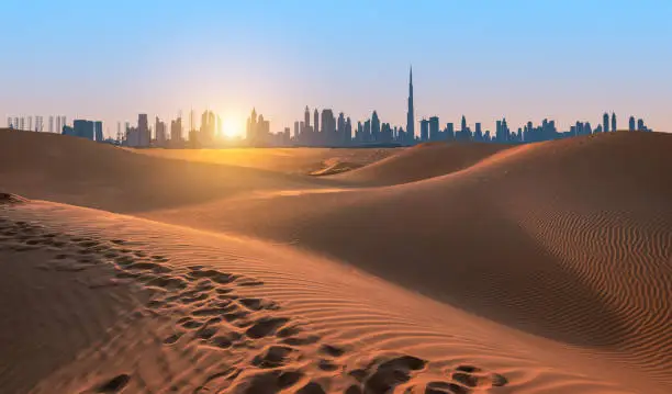Sand dunes of Dubai, silhouette of Dubai skyline at sunset. Beautiful travel image.