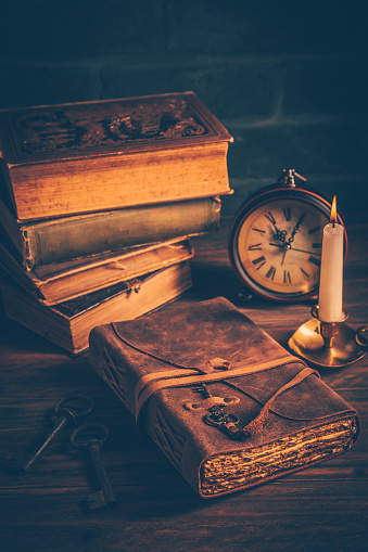 Old antique books with candle and vintage clock on wooden background