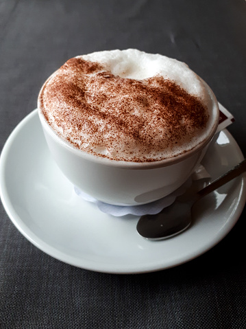 A cappuccino coffee with perfect froth served on a saucer in a coffee shop on neutral grey tablecloth