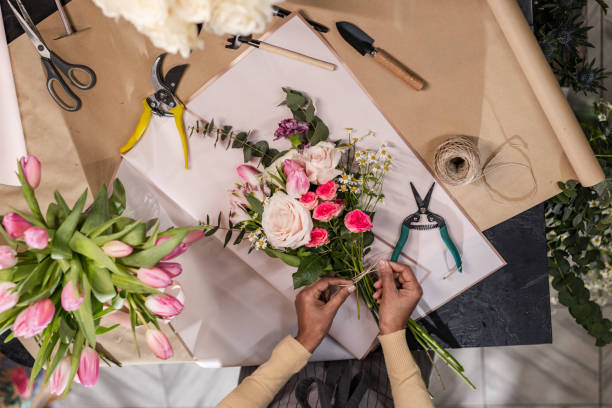 Creative occupation High-angle view of an unrecognizable woman arranging flowers on a wooden table. A woman's hands are creating a bunch of flowers. florist stock pictures, royalty-free photos & images