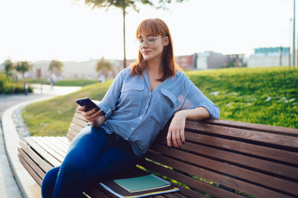 istock Charming woman in casual wear using smartphone while relaxing on bench at park 1460831508