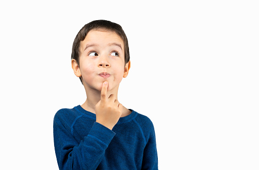Pensive kid looks away at copy space thinking isolated on a white background, funny kid lips hold finger near mouth conceiving some kind of joke, conceptual image