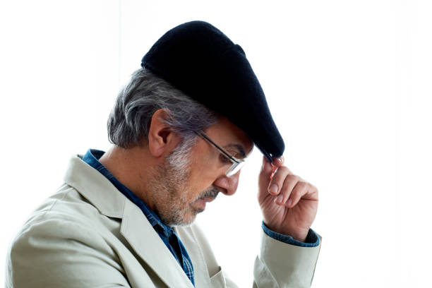 Portrait of bearded adult man in classic plaid flat cap, turtleneck and eyeglasses isolated on grey