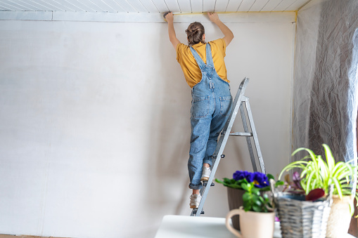 Young adult happy woman renovating the house, covering the walls with film