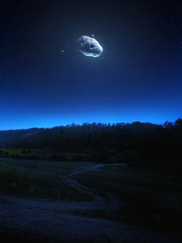 Large asteroid in the night sky. Surreal landscape with space stones over a valley and hills under a starry sky. Asteroids are approaching Earth.