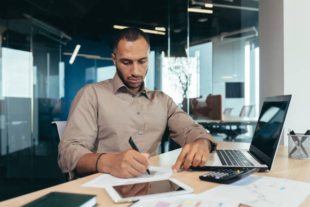 istock Serious thinking hispanic businessman working with documents and invoices inside office, man behind paper work, using laptop at work sitting at desk 1460835092