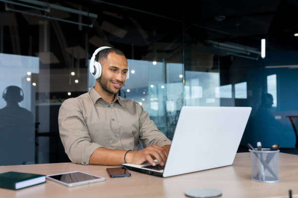 istock Young hispanic businessman in shirt working inside office using laptop at work, man with headphones listening to music and audio podcasts at work 1460835697