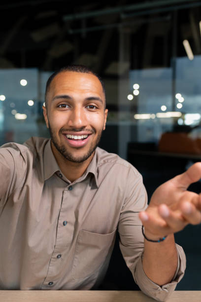 istock Video ringing, successful businessman looking at smartphone camera talking remotely with colleagues, Hispanic man smiling at work inside office, webcam view pov vertikal. 1460836355