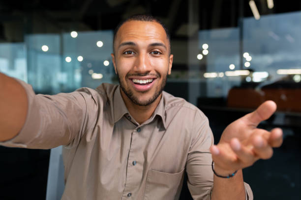 istock Video ringing, successful businessman looking at smartphone camera talking remotely with colleagues, Hispanic man smiling at work inside office, webcam view pov 1460836544