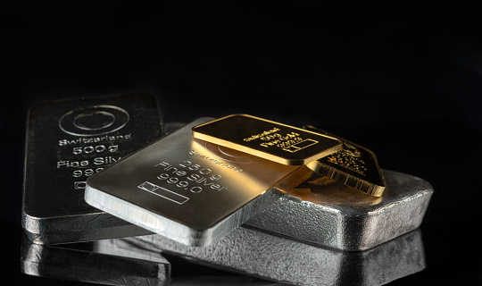 Gold and silver bars of various weights on a dark background. Selective focus.