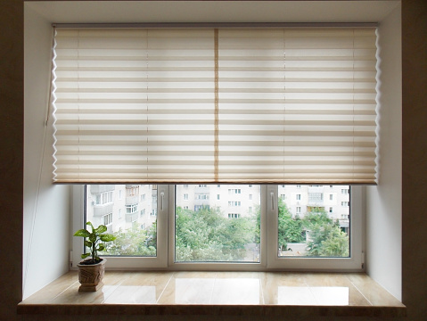 Pleated blinds XL, beige color, with 50mm fold closeup in the window opening in the interior. Home blinds - modern bottom up privacy shades half raised on apartment windows.
