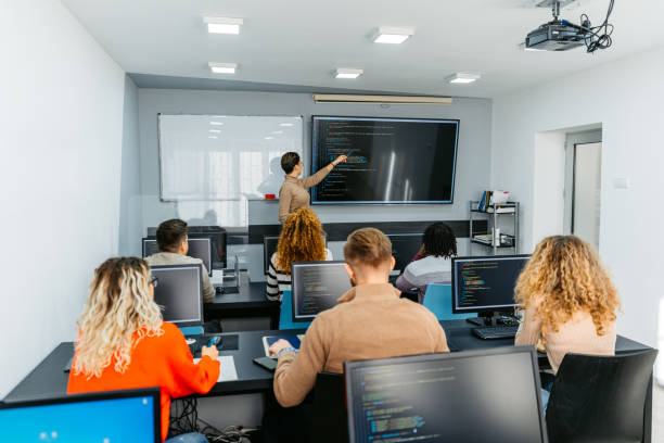 Young Female Teacher Teaching A Programing Class Young female teacher teaching young students a programming class in the classroom. teacher projector stock pictures, royalty-free photos & images