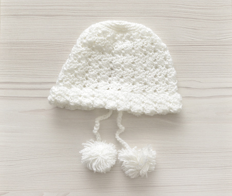 Closeup of a hand made, crocheted baby toque on a whitewashed wood background.