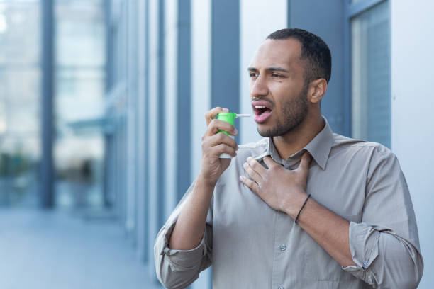 un joven latinoamericano se aclara la garganta con un inhalador y un medicamento. se para afuera - coughing illness men latin american and hispanic ethnicity fotografías e imágenes de stock