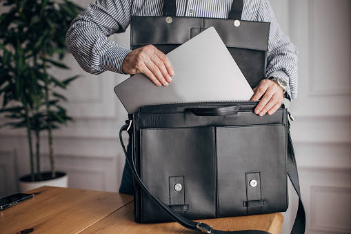 Unrecognizable elegant businessman putting laptop modern leather bag.