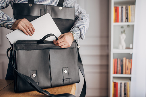 Unrecognizable elegant businessman putting laptop modern leather bag.