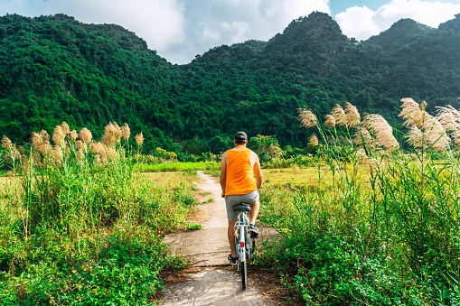 white european male tourist bicycling in Vietnam, Cat Ba Island\nkarst formation in the background