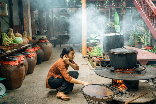 young vietnamese woman is cooking on open fire in restaurant in north vietnam
