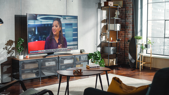Living Room Television Showing TV News Programme with Two Presenters Talking and Joking on TV. Live Broadcast of The Popular Talk Show. Cozy Apartment Living Room with Loft Interior.