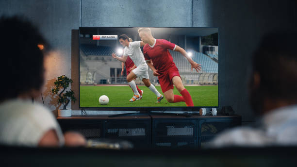 un couple noir regarde un match de football professionnel à la télévision, assis sur un canapé à la maison le soir. les fans de football de petit ami et de petite amie regardent des sports. vue arrière floue gros plan de nuit. - regarder la télévision photos et images de collection