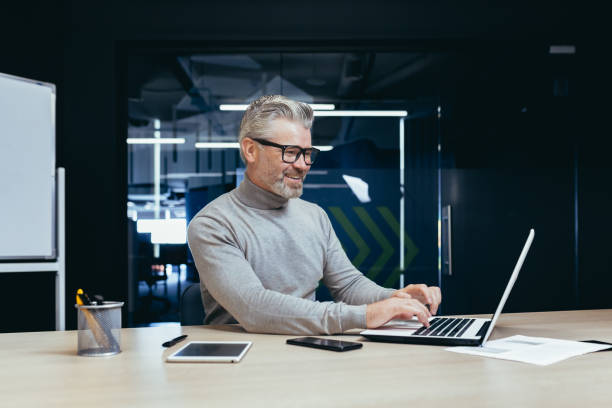 istock Cheerful and smiling mature businessman working inside office, senior gray haired man using laptop at workplace smiling satisfied with good results achievement 1460851739