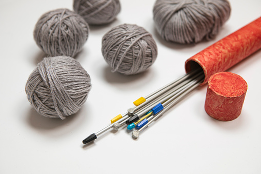 Knitting background. Set of Knitting needles in red box, bunch of grey yarn. Wool balls on white background, retro style knitting set. Hobby, winter time leisure activities.
