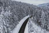 Snow-covered trees in the forest and asphalt road line in the mountains. Winter landscape in the mountains. Aerial drone panoramic photo.