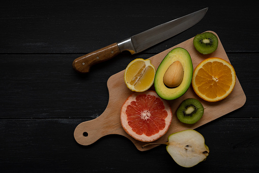 Half cut fruits and vegetables on cutting board with knife as a vegan background