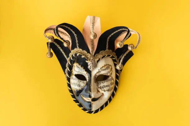 Venetian carnival mask on the yellow background. Full-head black characteristic mask with golden decoration. Flat lay. Copy space for a free text