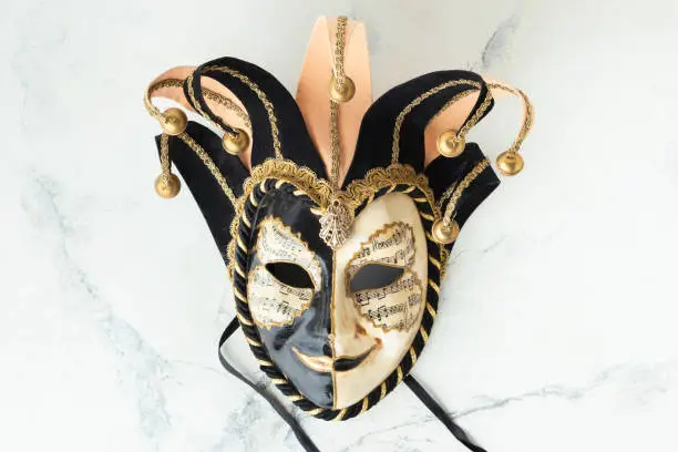 Venetian carnival mask on the white marble background. Full-head black characteristic mask with golden decoration. Flat lay. Copy space for a free text