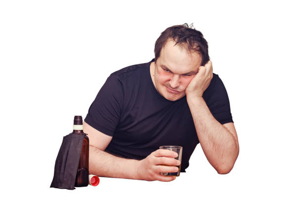 怒っている男は、白い背景に台所のテーブルにウイスキーのボトルを持って座ってアルコールを飲む。流行、隔離、封鎖中のアルコール依存症の問題 - eastern european caucasian one person alcoholism ストックフォトと画像