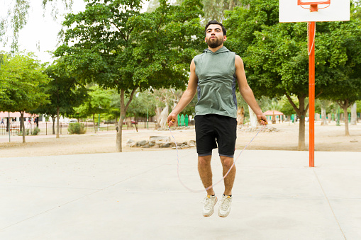 Fitness hispanic man working out and doing cardio exercises while jumping rope outdoors