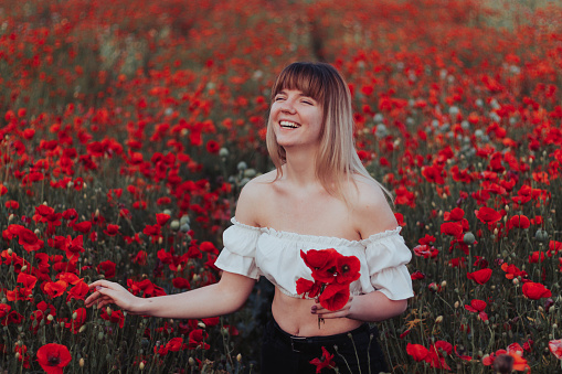 Young Woman Collecting Red Poppy Flowers in her hand on a Poppy Field