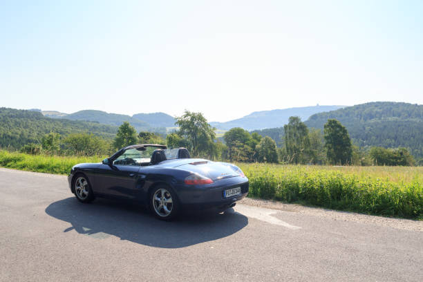 gersfeld, niemcy - 23 lipca 2021 r.: niebieski roadster porsche boxster 986 z panoramą wasserkuppe w górach rhön. samochód to dwumiejscowy samochód sportowy z silnikiem umieszczonym centralnie produkowany przez porsche. - germany landscape nissan roadster zdjęcia i obrazy z banku zdjęć