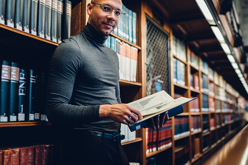 Half length portrait of intellectual professor of history in bifocal eyewear looking at camera while holding literature book in hand for making research of information for new science publication