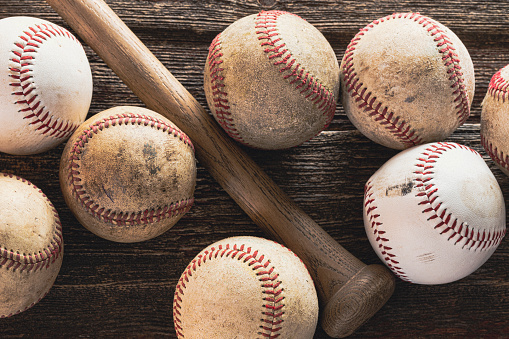 An old wood baseball bat with a collection of used baseballs.