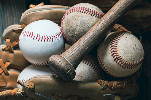 A collection of baseballs in a vintage baseball glove with a wood bat.