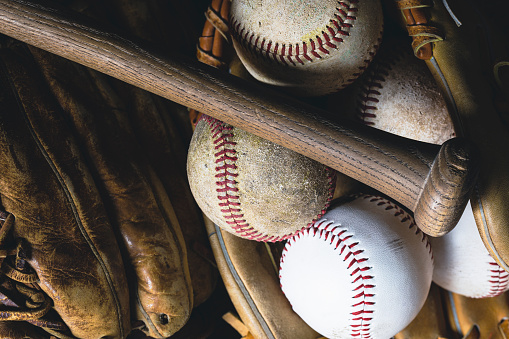 A collection of baseballs in a vintage baseball glove with a wood bat.