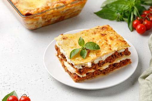 Portion of Homemade Italian lasagna. Delicious Lasagne with bolognese meat sauce and basil on white plate. Hot Tasty Lasagna with cheese.