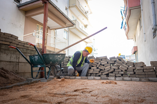 Man in gloves lays paving stones in layers on garden pathway.