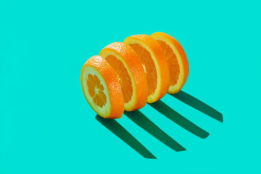 Sliced orange in bright light minimalist on a blue table. Slices of juicy fresh orange fruit aligned on a vibrant colored background