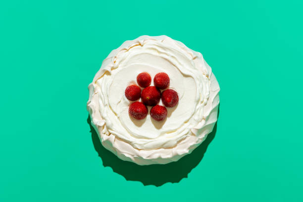 Pavlova with strawberries, above view on a green background. Homemade pavlova cake, topped with fresh strawberries, minimalist on a green table. Delicious meringue cake filled with whipped cream. pavlova stock pictures, royalty-free photos & images